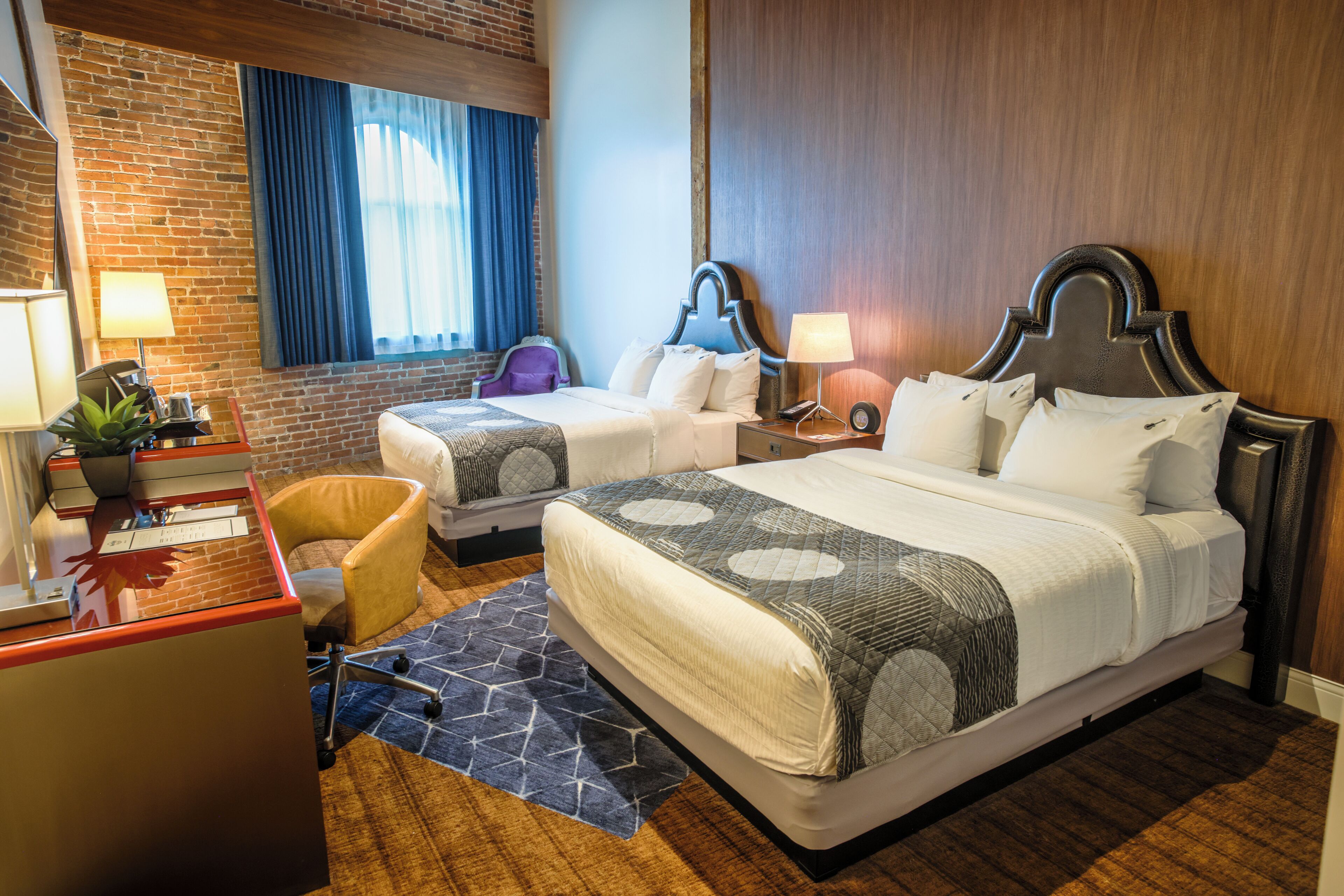 Una habitación de hotel con dos camas, un escritorio, una silla y una ventana con cortinas.
