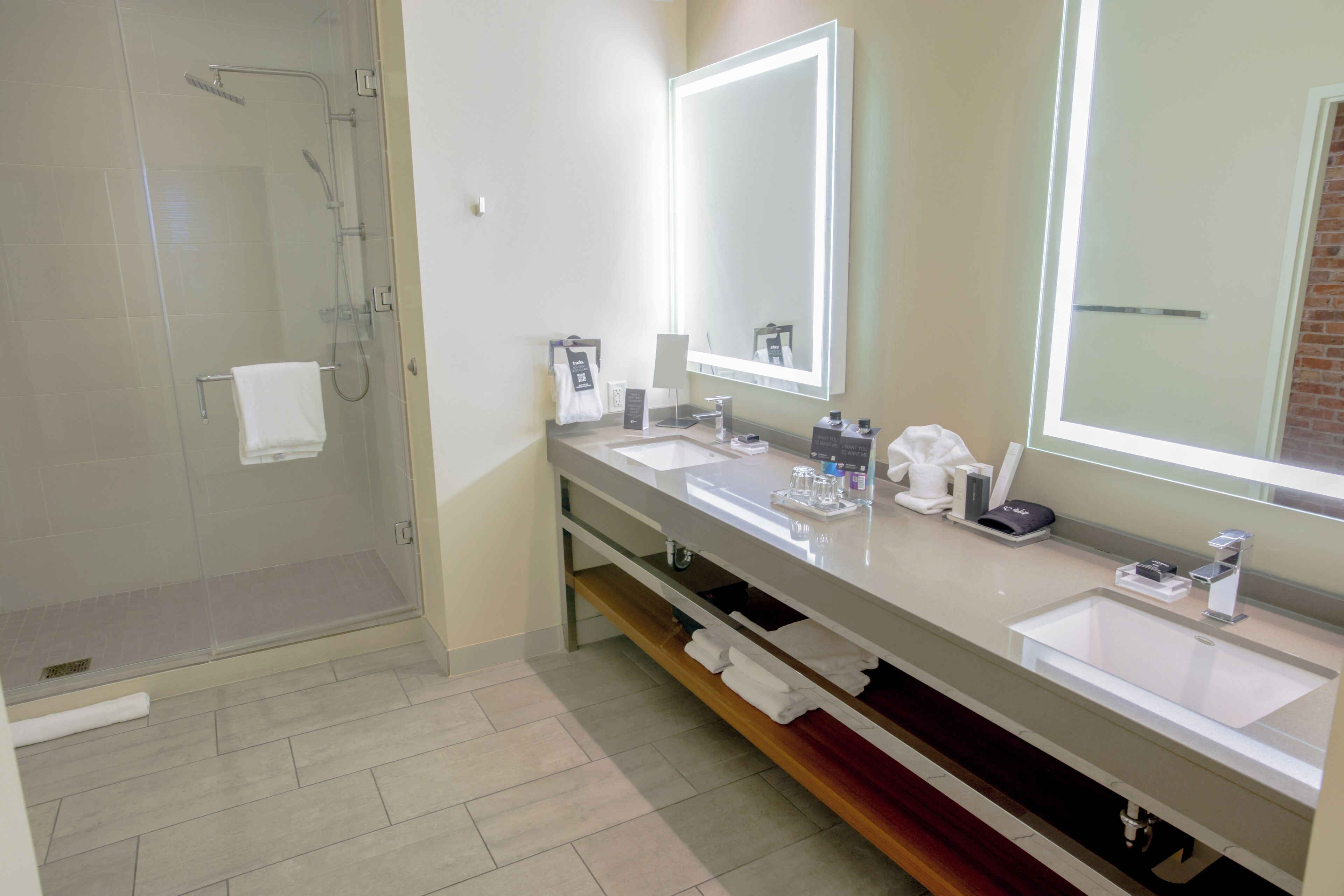 A modern bathroom with a glass shower enclosure, two sinks, and a large mirror with integrated lighting.