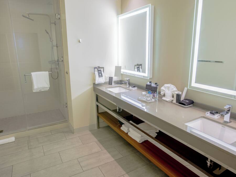 A modern bathroom with a glass shower enclosure, two sinks, and a large mirror with integrated lighting.
