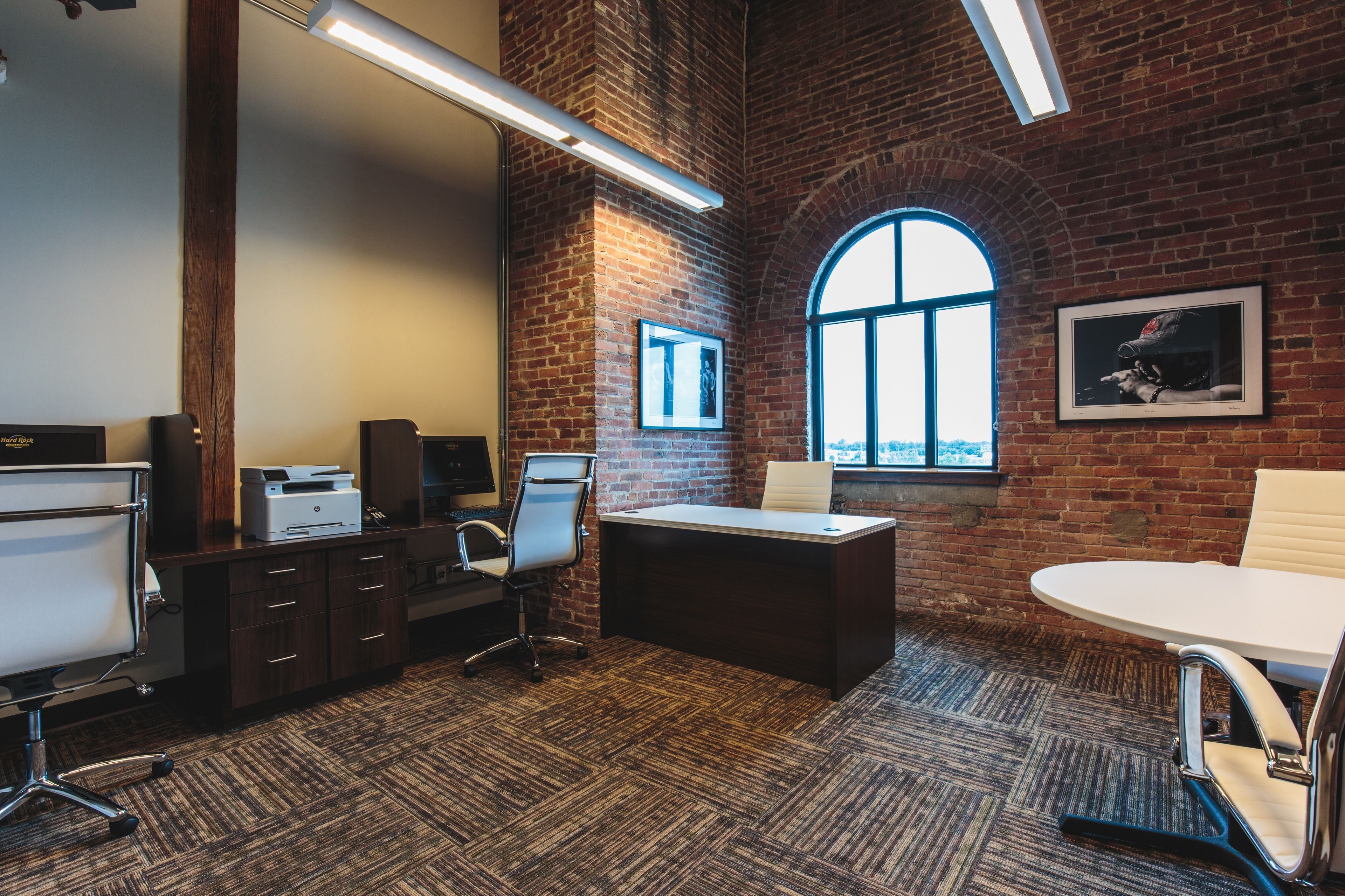 A modern office with a brick wall, a large window, and a desk with a chair.