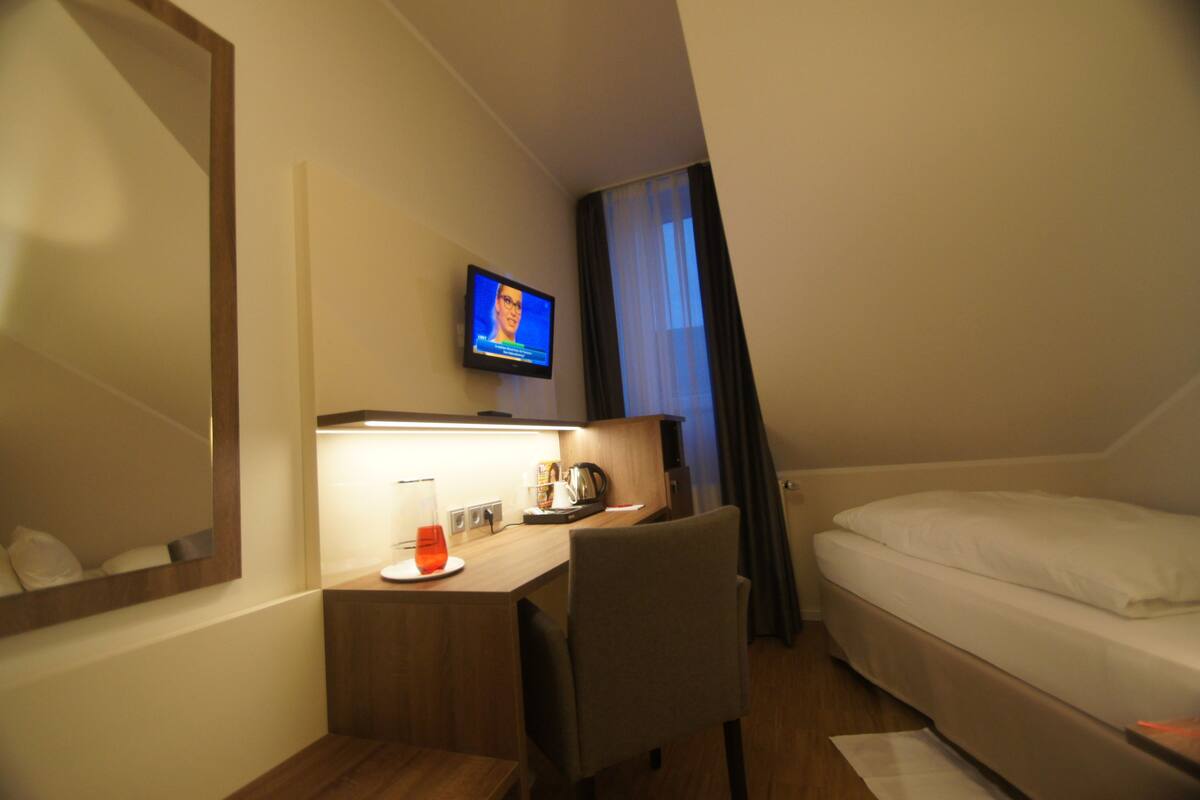 Ein Hotelzimmer mit Bett, Schreibtisch mit Stuhl, Fernseher und einem Fenster mit Vorhängen.