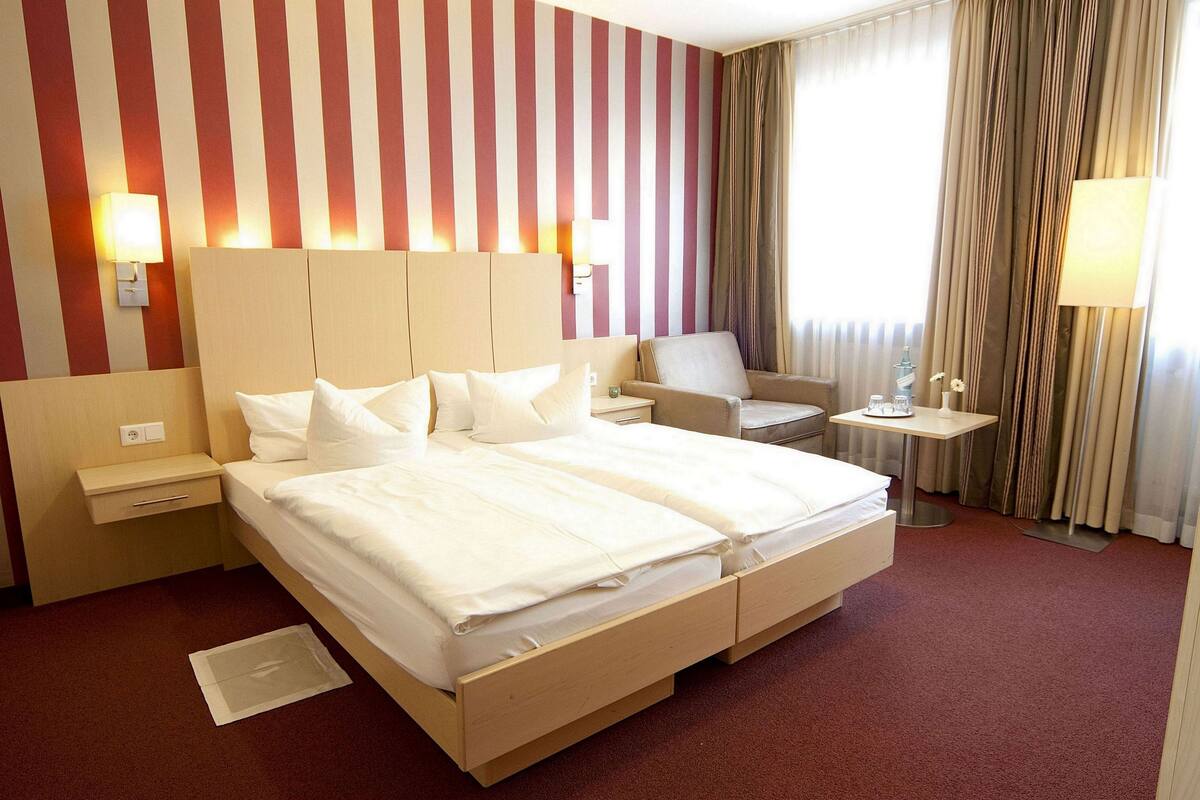 Ein Hotelzimmer mit einem großen Bett, Nachttischen, einem Sessel und einem kleinen Tisch mit einer Lampe.
