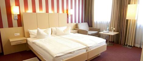 A hotel room with a large bed, bedside tables, a chair, and a small table with a lamp.