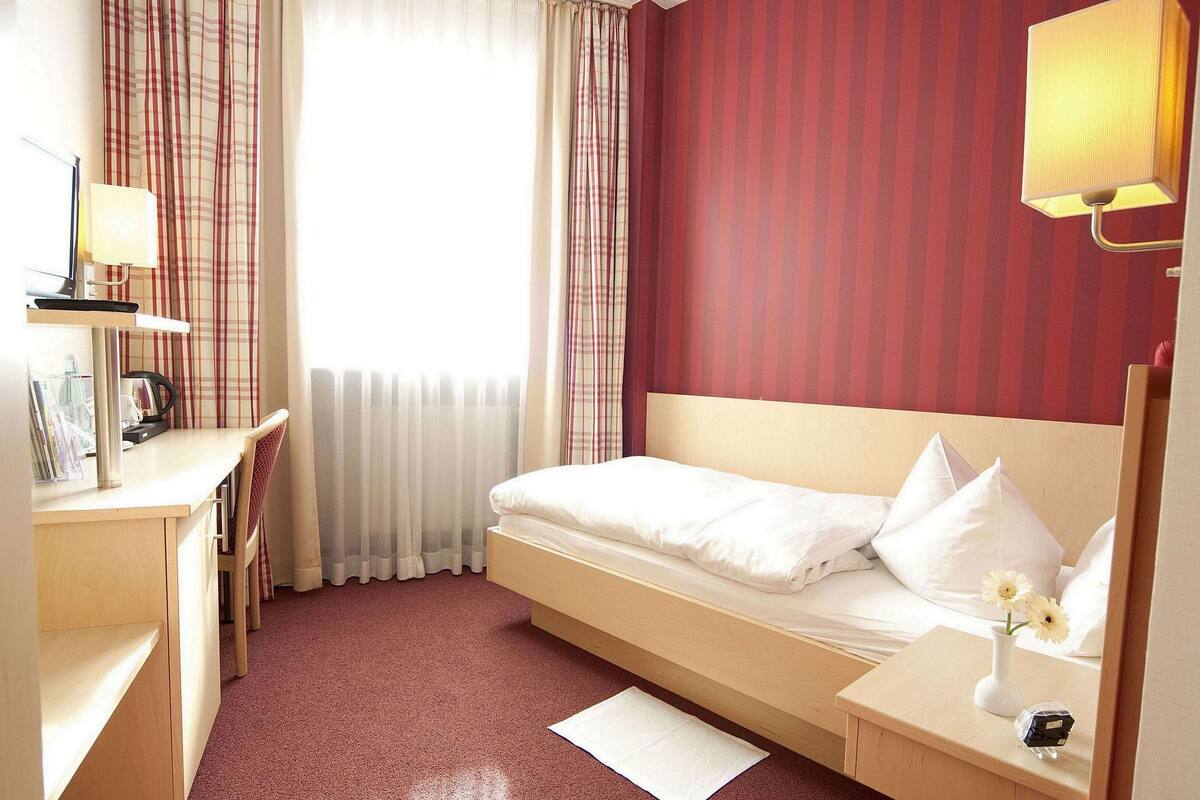 Ein Hotelzimmer mit Bett, Nachttisch, Lampe und Schreibtisch mit Stuhl.