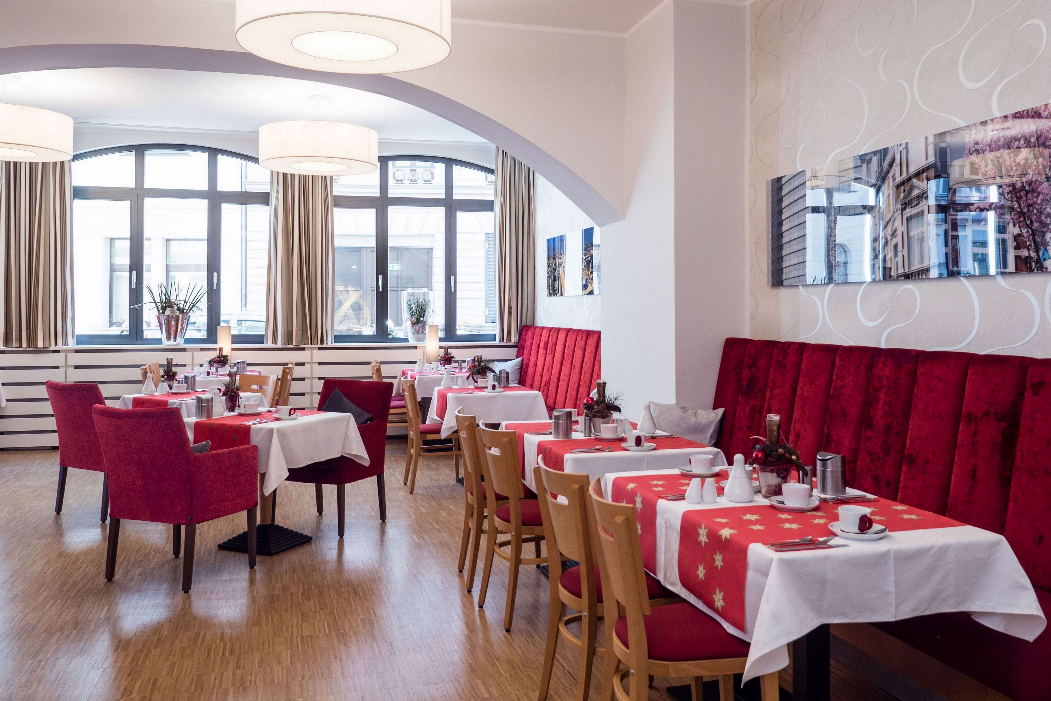 Un restaurant avec des banquettes et des tables recouvertes de tissu rouge, et des nappes blanches.