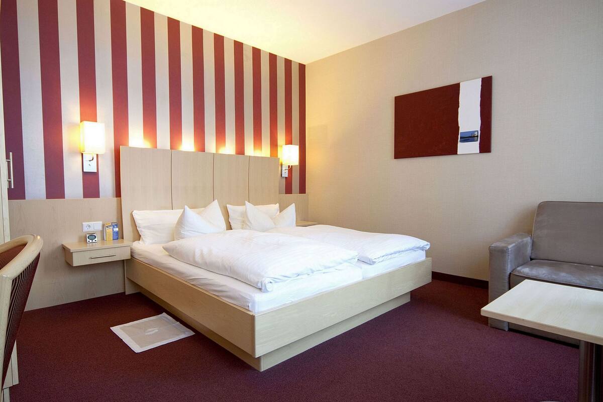 Ein Hotelzimmer mit einem großen Bett, Nachttischen, einem Sessel und einem kleinen Tisch.
