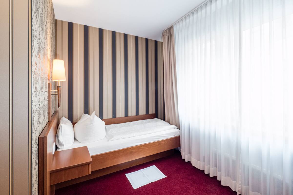 Ein Hotelzimmer mit einem hölzernen Bett, gestreifter Tapete, einer Nachttischlampe und transparenten Vorhängen.