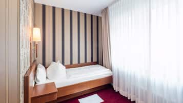 Une chambre d’hôtel avec un lit en bois, un papier peint à rayures, une lampe de chevet et des rideaux transparents.