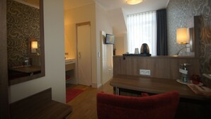 Een hotelkamer met een houten bureau, een rode stoel, een televisie en een spiegel.
