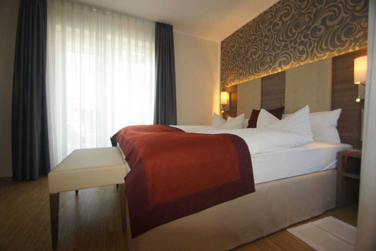 Ein Hotelzimmer mit einem großen Bett, einem Nachttisch und einem Fenster mit Vorhängen.