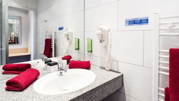 Baño de hotel con un lavamanos blanco, toallas rojas, un secador de pelo y un tendedero para toallas.