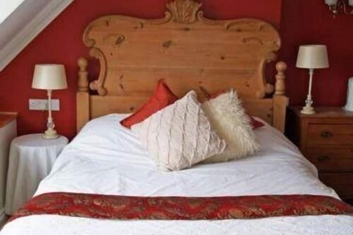 A neatly made bed with a wooden headboard, white bedding, and a red and white patterned throw.