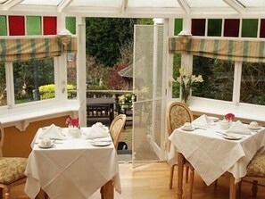 A conservatory with two dining tables set for a meal, surrounded by windows with decorative panels. - Tower House 1066 (St Leonards-On-Sea)