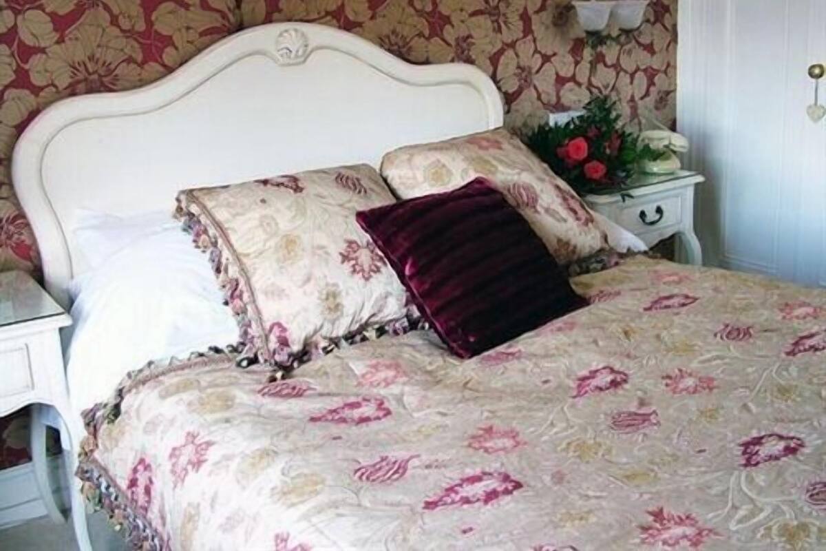 A bedroom with a floral-patterned bedspread, a white headboard, and a nightstand with a vase of flowers.