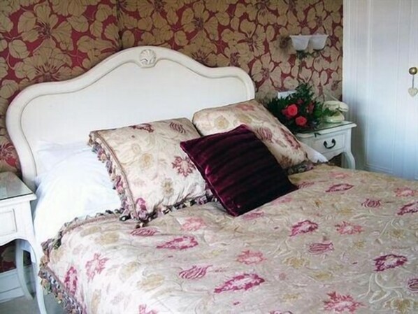 A bedroom with a floral-patterned bedspread, a white headboard, and a nightstand with a vase of flowers.