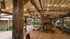 Un patio al aire libre con mesas y bancos de madera, macetas colgantes y suelo de piedra.