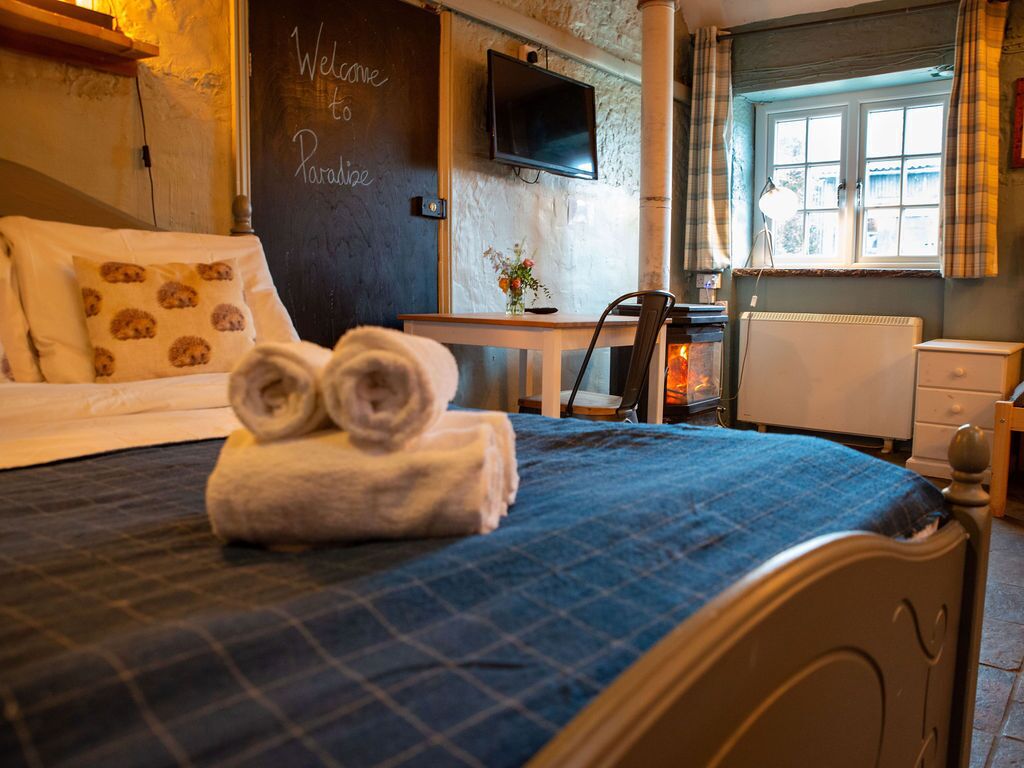 Ein gemütliches Zimmer mit einem Bett, einem Tisch, einem Sessel, einem Kamin und einem an der Wand befestigten Fernseher.