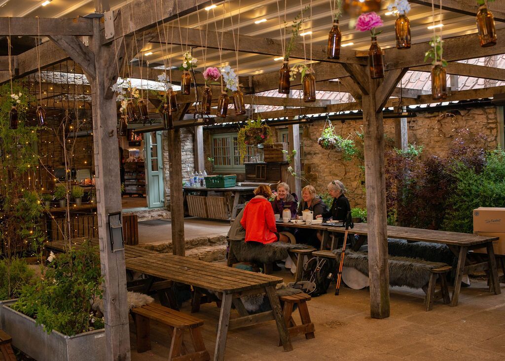 Un jardin intérieur avec des tables et des bancs en bois, des compositions florales suspendues et des murs en pierre.