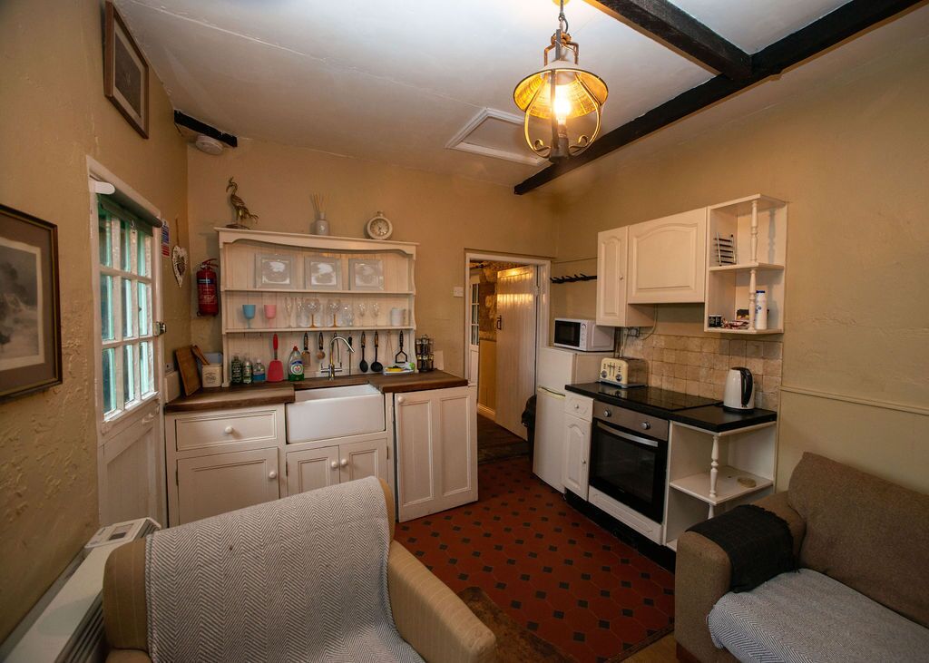 A compact kitchen with white cabinets, a microwave, and a toaster. There is a red patterned floor and a hanging light fixture.