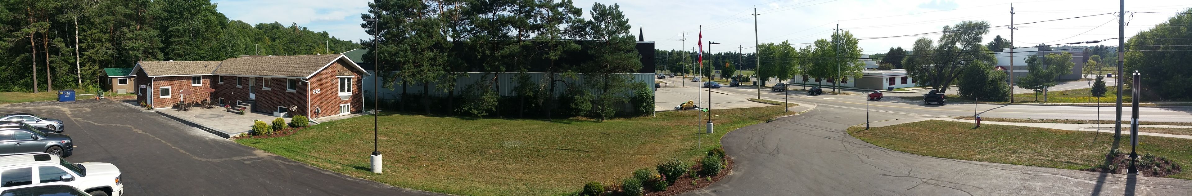 A building with a brick exterior, a parking lot with several cars, and a grassy area with trees.