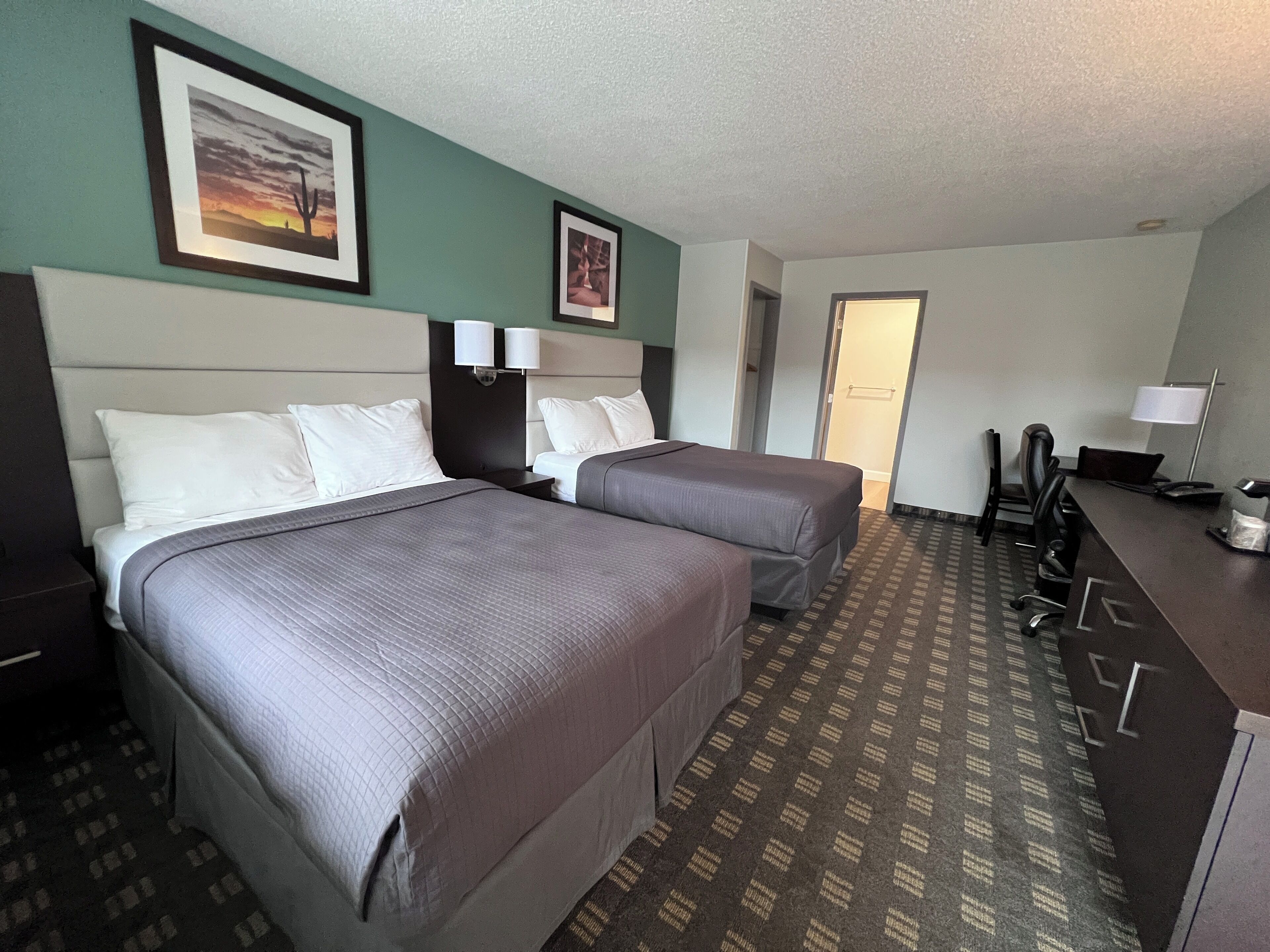 Habitación de hotel con dos camas, un escritorio, una silla y una puerta que da a otra habitación.