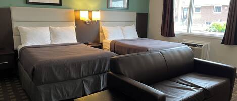 A hotel room with two beds, a sofa, a small table, and two wall-mounted lamps.