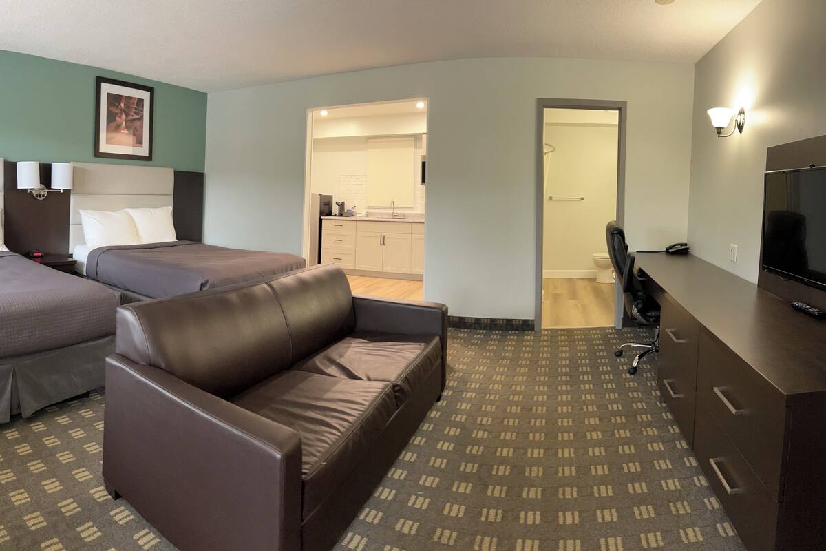 Habitación de hotel con dos camas, un sofá, un televisor y una kitchenette.