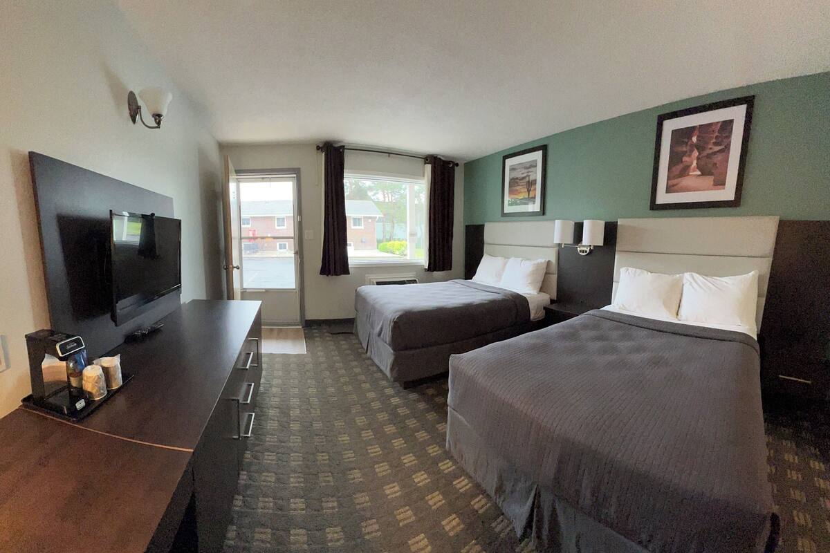 Habitación de hotel con dos camas, televisión, escritorio y ventana con cortinas.