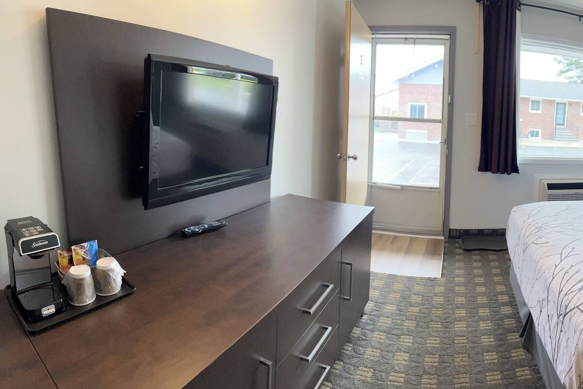 Una habitación de hotel con cama, televisión, escritorio con cafetera y una silla.