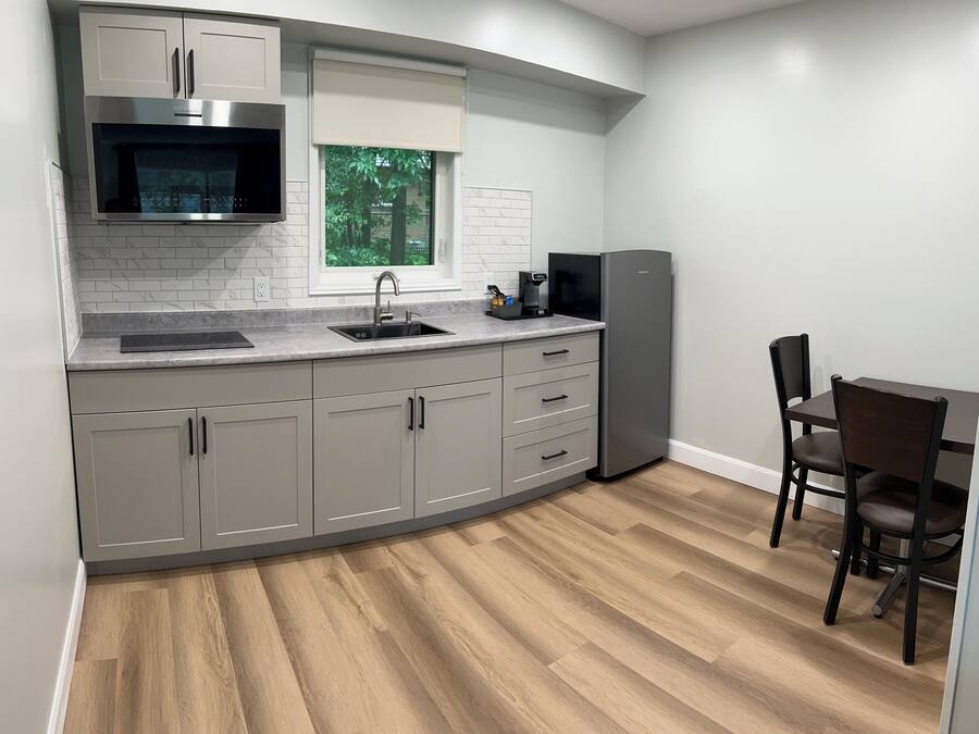 A modern kitchen with grey cabinets, a stainless steel microwave, a sink, and a refrigerator.
