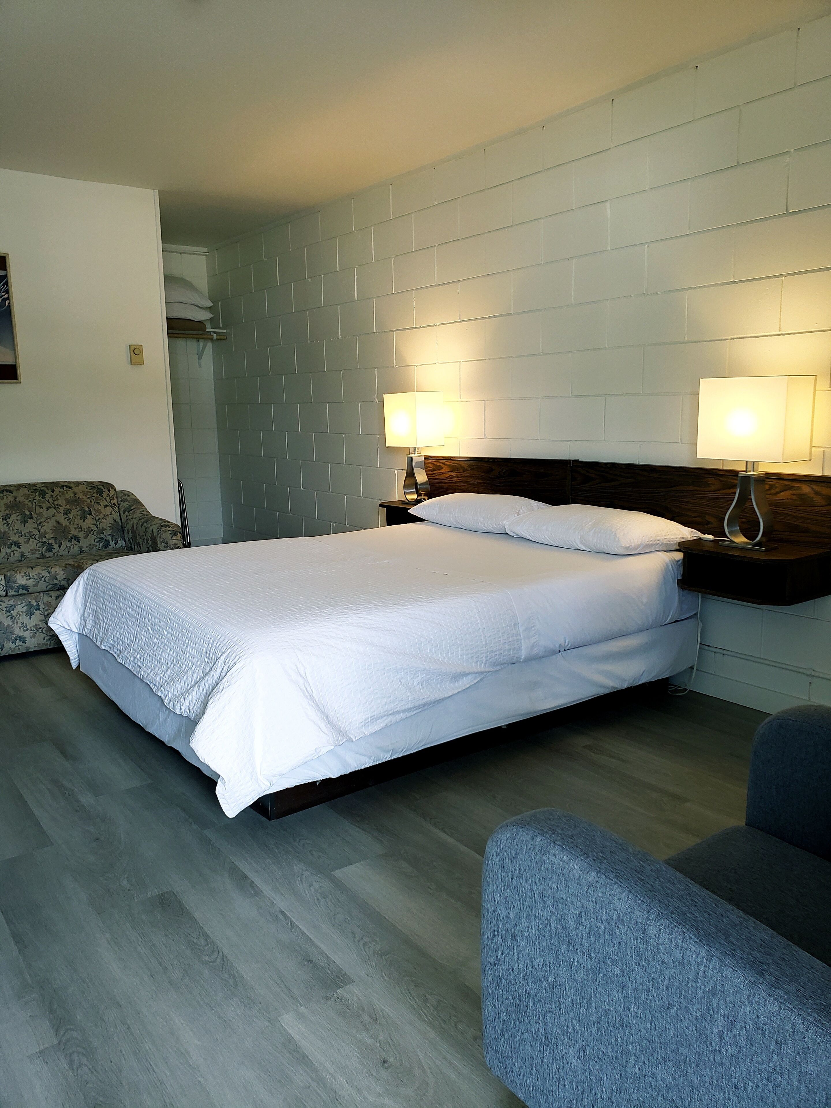Un dormitorio ordenado con cama, dos lámparas de noche, una silla y un sofá.