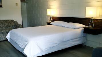 Un dormitorio ordenado con cama, dos lámparas de noche, una silla y un sofá.