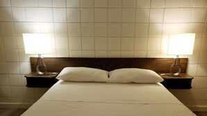 Ein ordentlich bezogenes Bett mit zwei Kissen und je einer Nachttischlampe auf Holznachttischen.