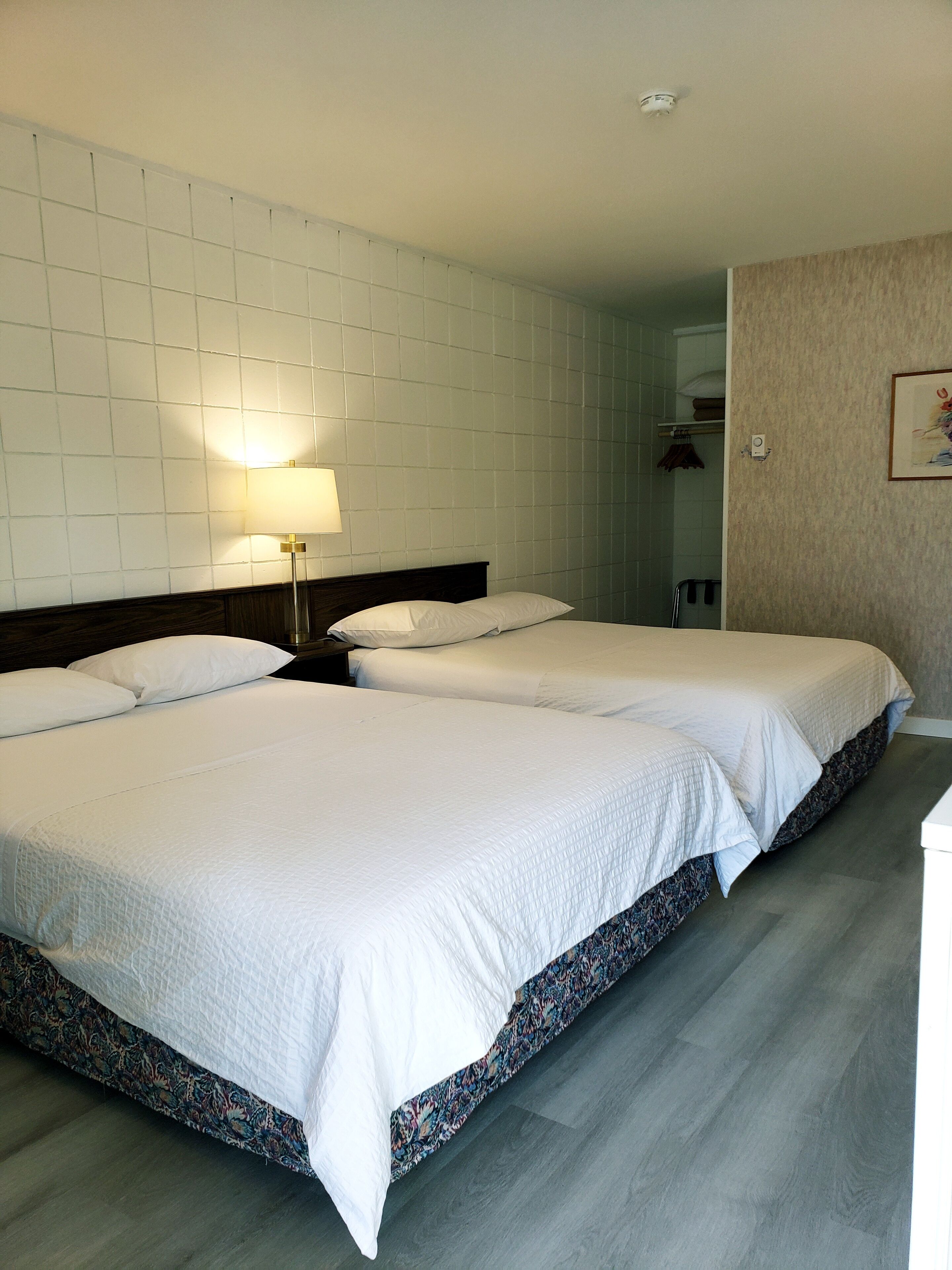 Une chambre d’hôtel avec deux lits, une table de chevet avec une lampe, un miroir et un luminaire fixé au mur.