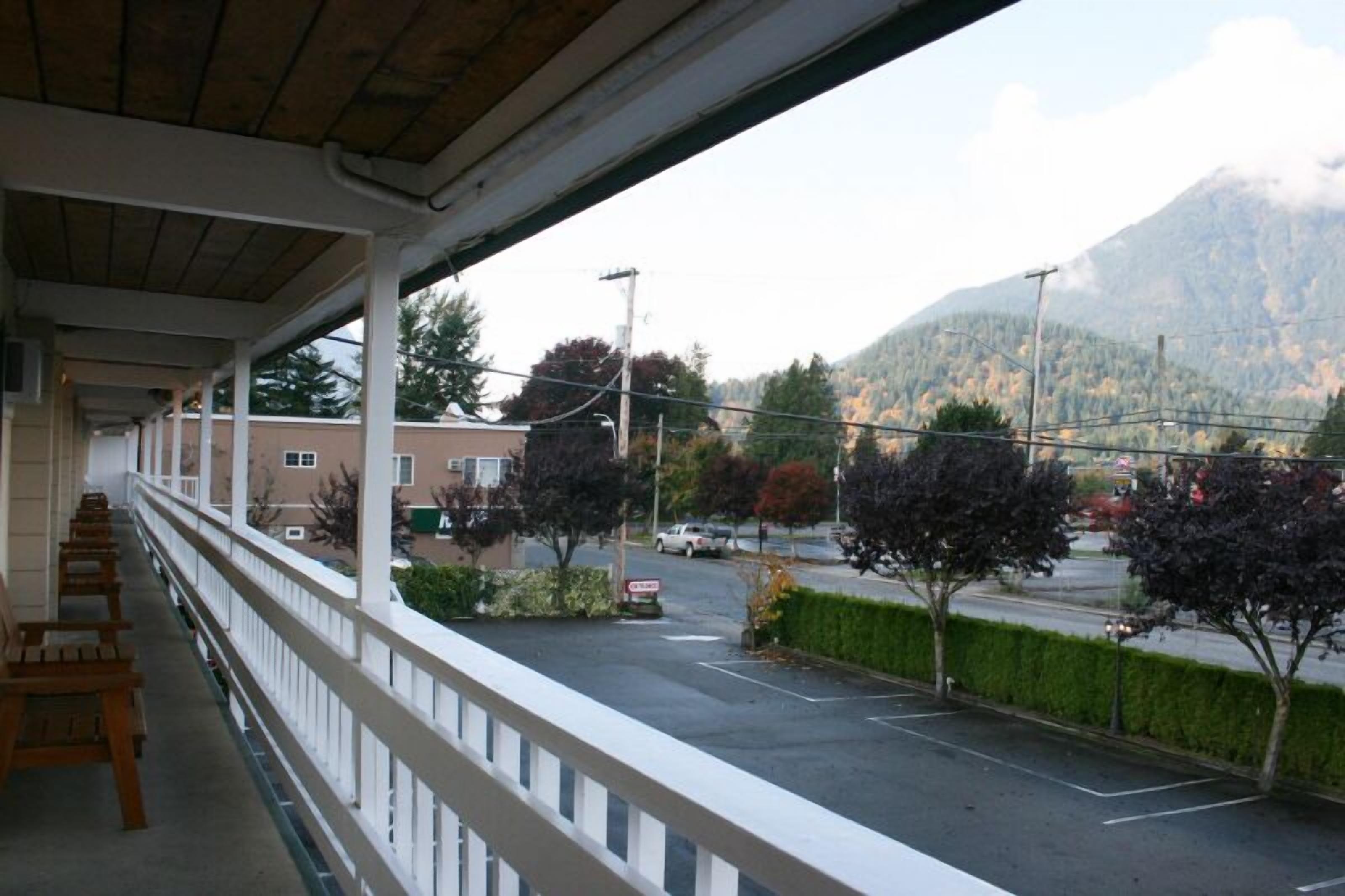 A covered balcony with a view of a parking lot and a mountain in the background.