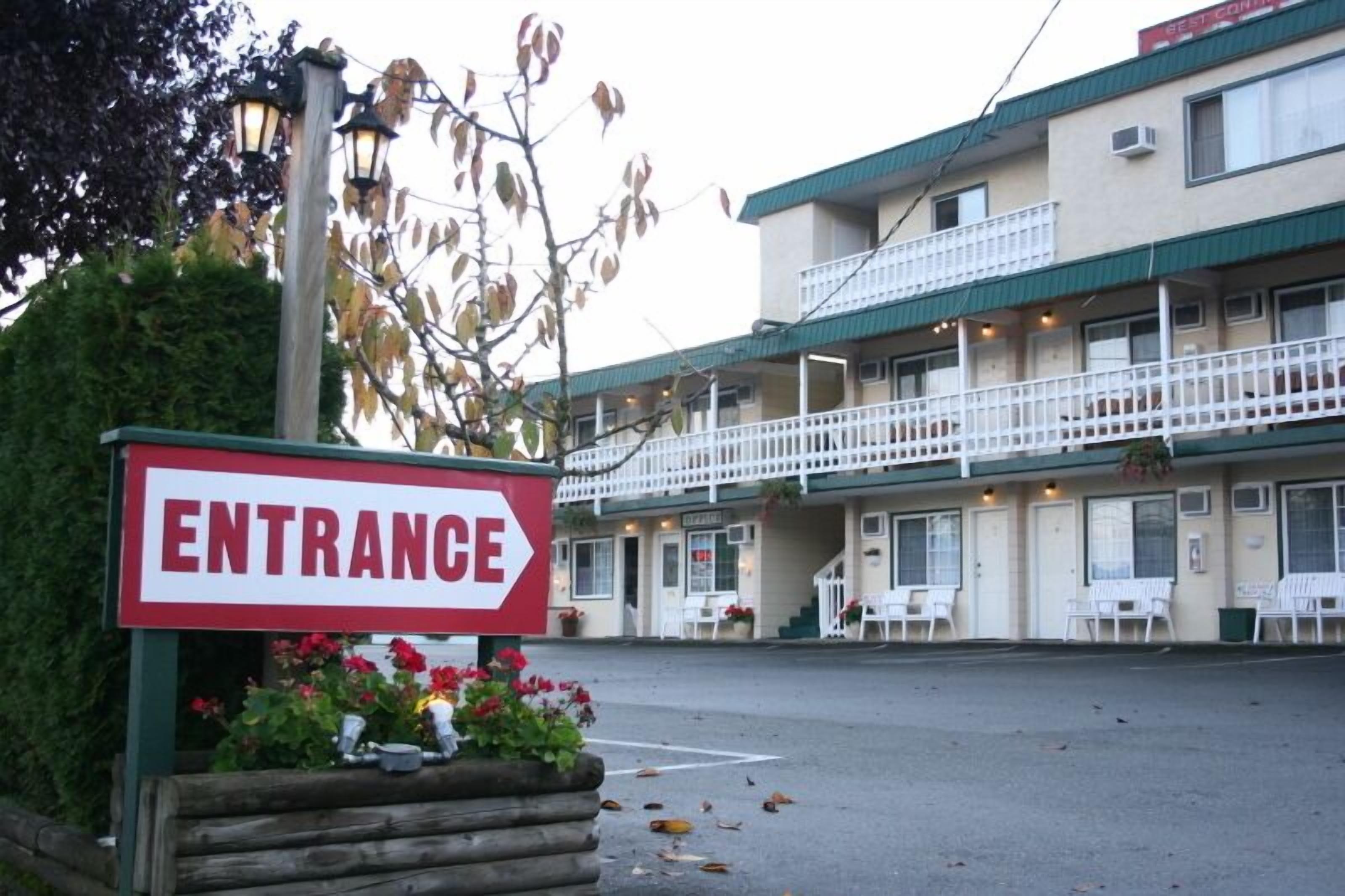Un motel con letrero de entrada, asientos al aire libre y un edificio de dos pisos con balcones.
