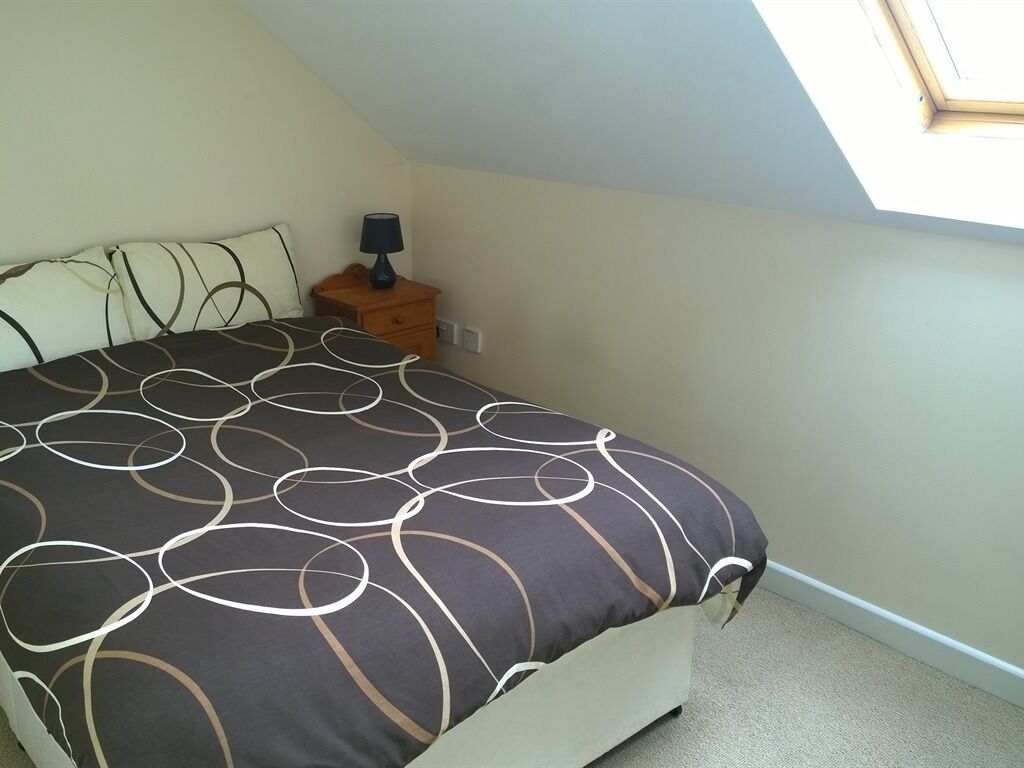 Une chambre à coucher avec un lit, une table de chevet, une lampe et une lucarne.