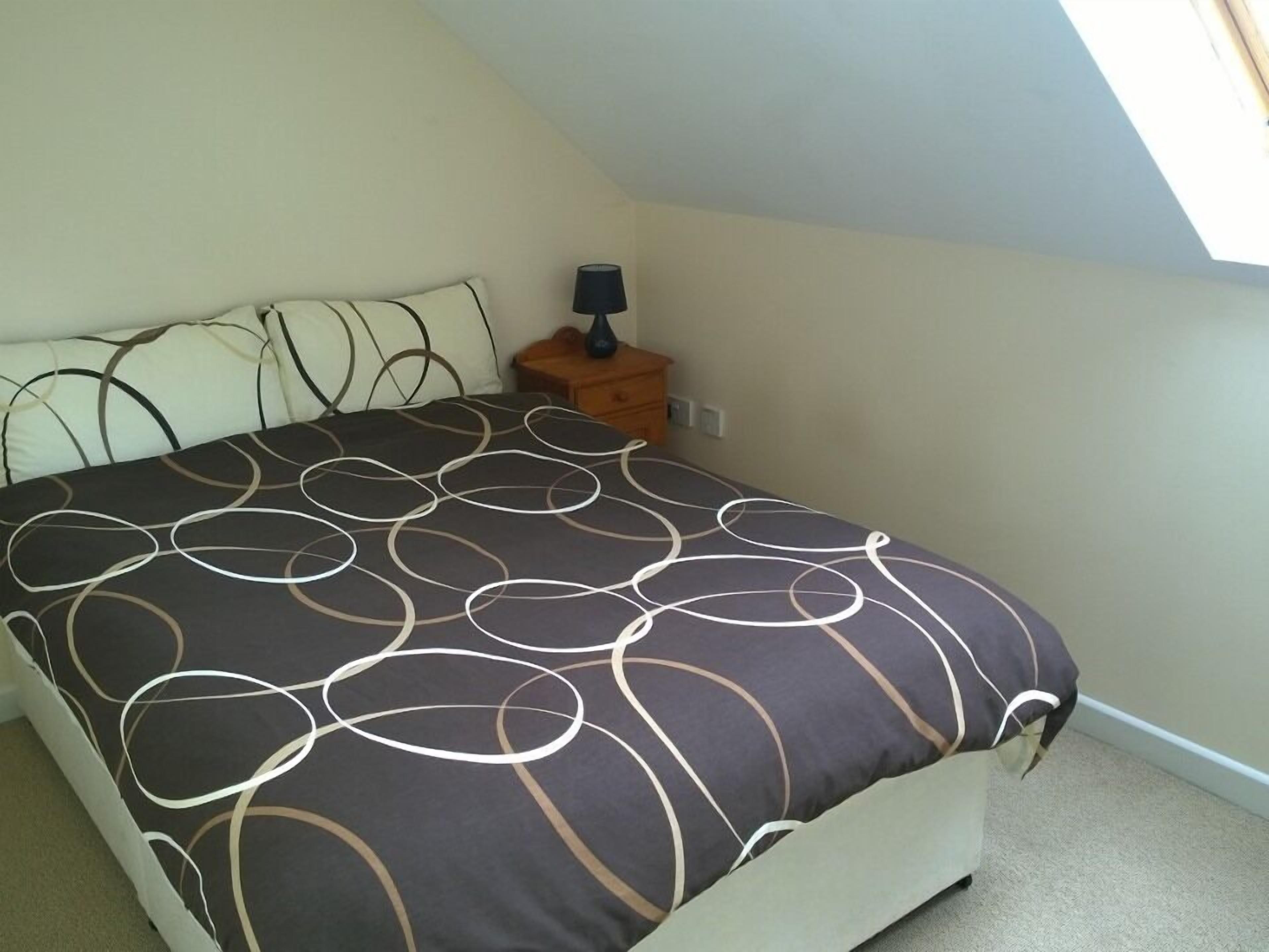 Ein Schlafzimmer mit einem Bett, einem Nachttisch, einer Lampe und einem Fenster.