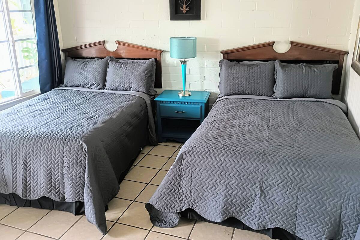 Una habitación doble con dos camas, una mesita de noche con lámpara, un adorno en la pared y una ventana con cortinas.