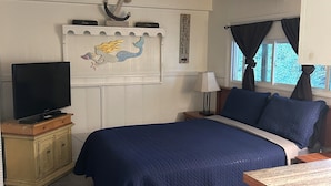 Une chambre à coucher avec un lit, un téléviseur posé sur un meuble, une table de chevet, une lampe et un élément de décoration murale.