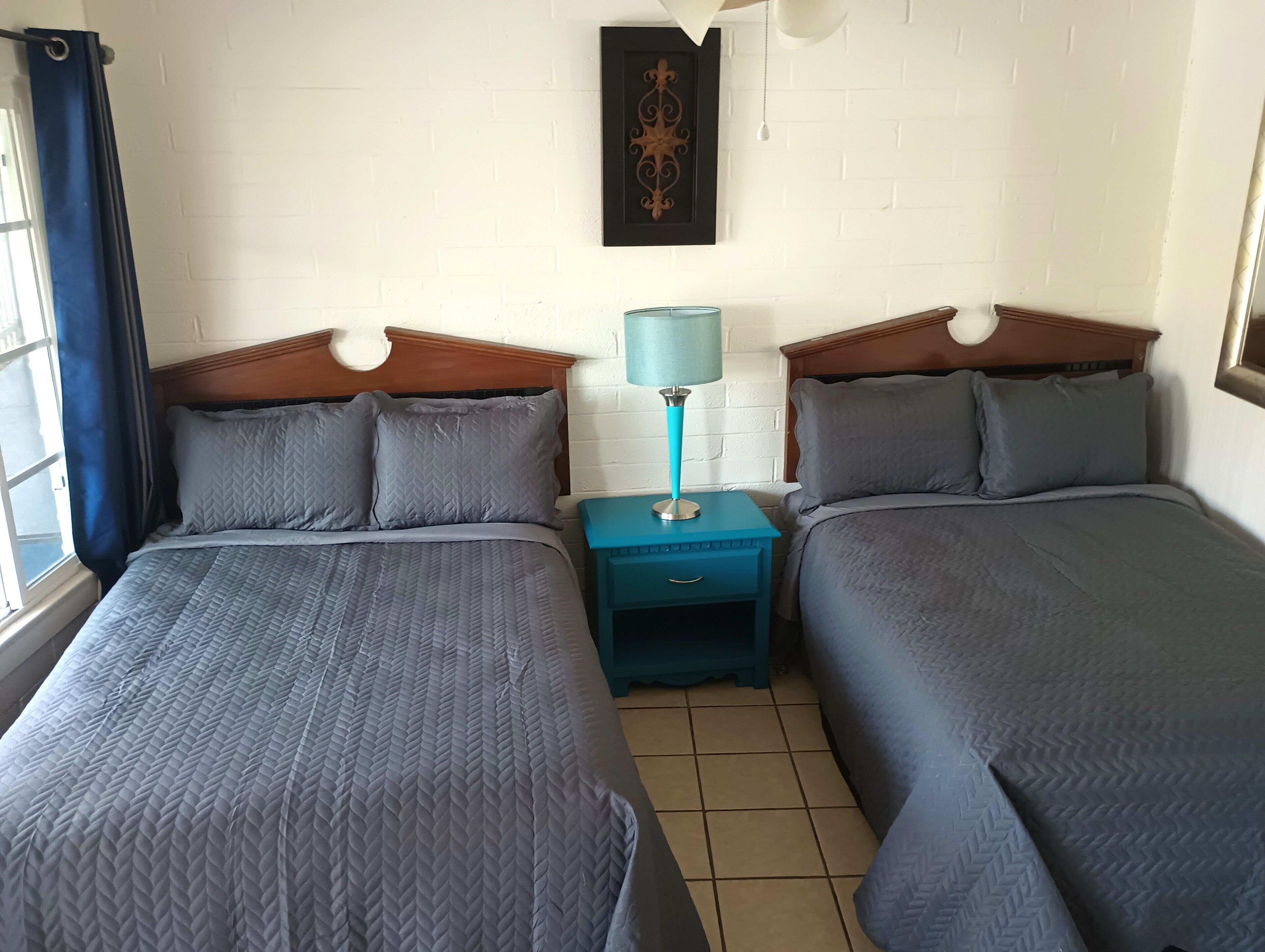 Habitación doble con dos camas, una mesita de noche, una lámpara y un adorno en la pared.