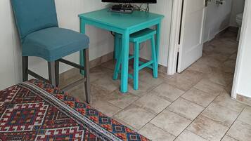 Una habitación con una televisión sobre un mueble bajo, una silla color turquesa, una mesita y una alfombra estampada.