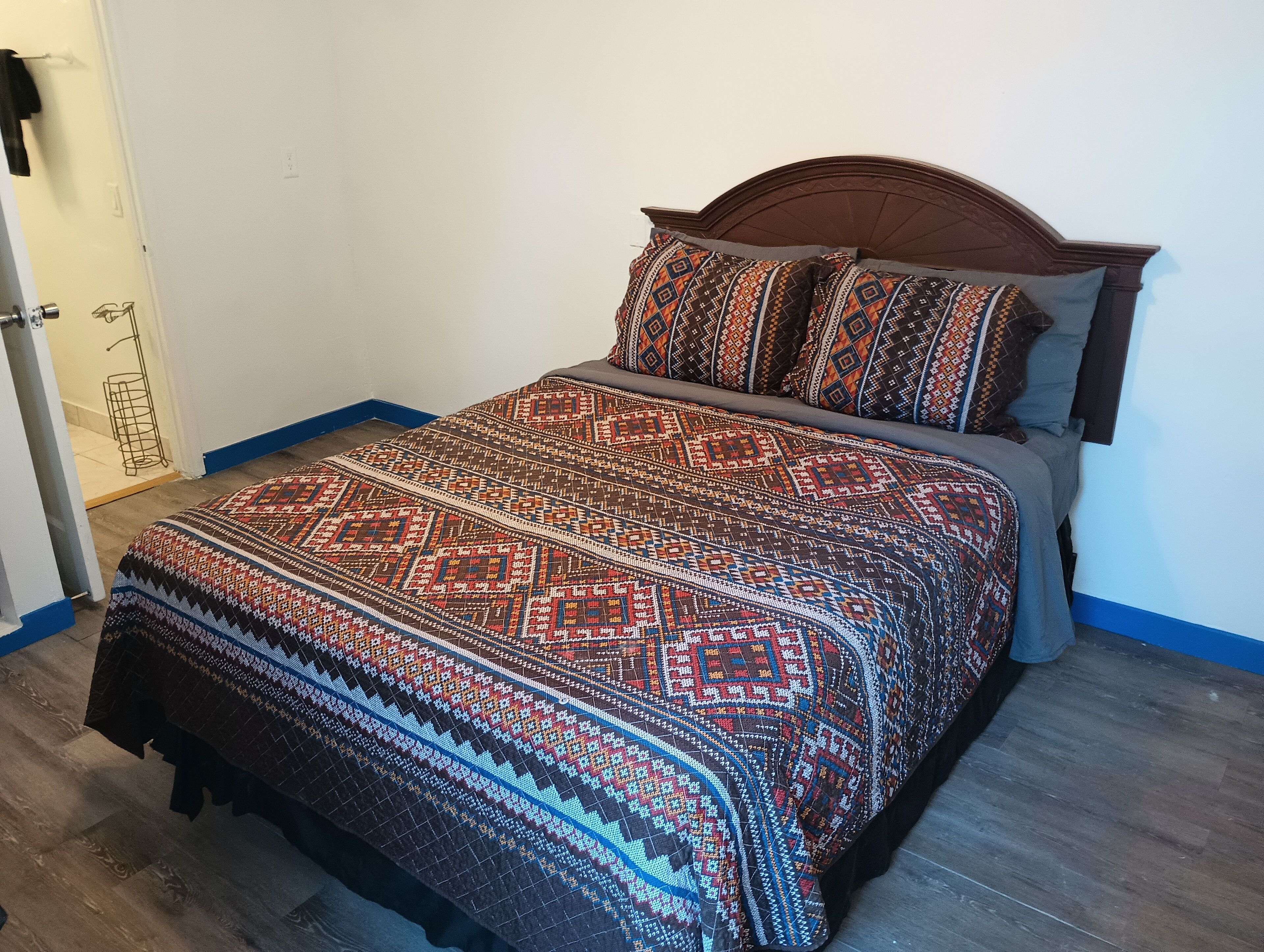 Una cama con una colcha estampada y almohadas a juego, un cabecero de madera y una puerta a la izquierda.