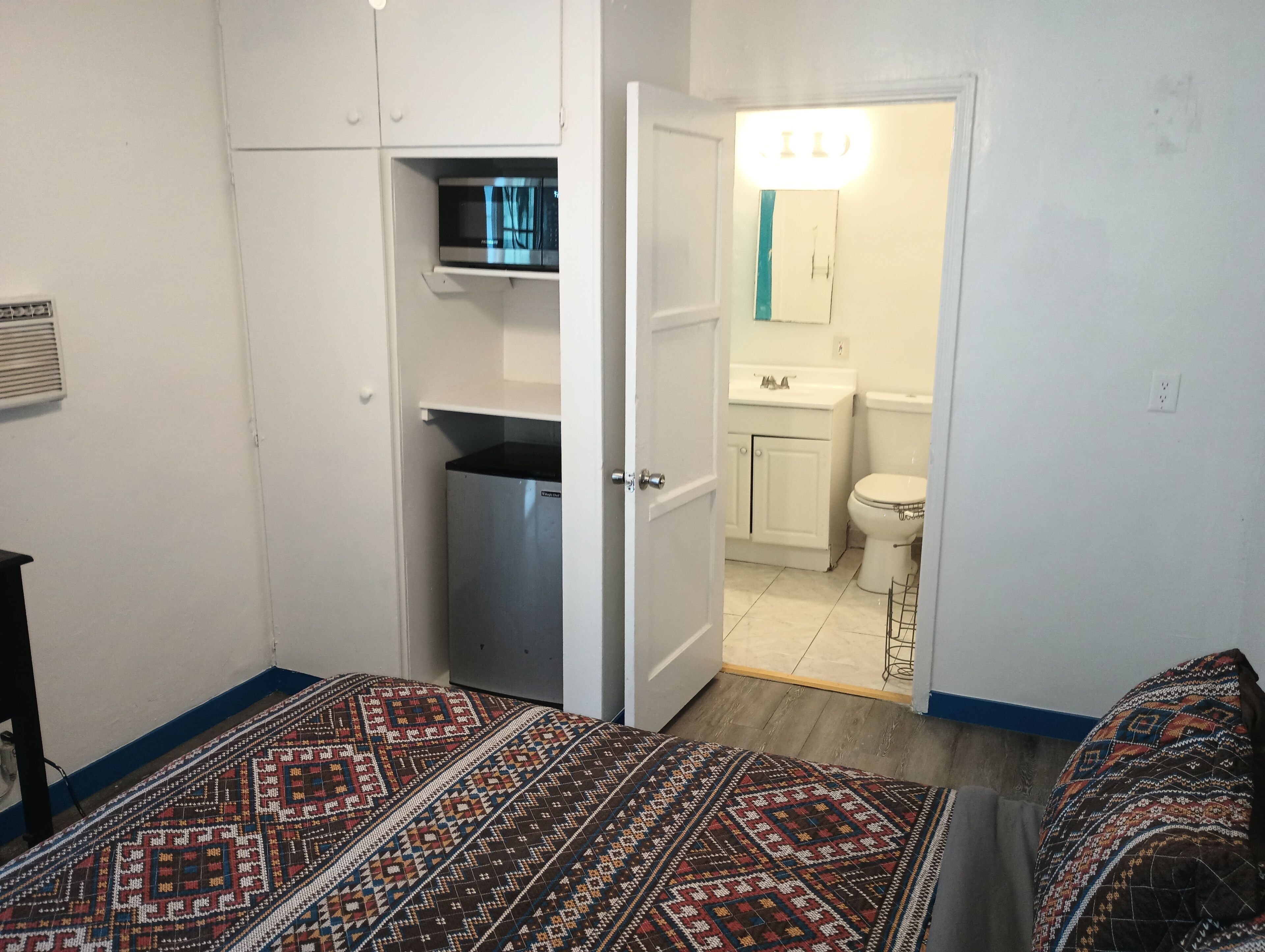 Une chambre à coucher avec un lit, une armoire et une salle de bain visible à travers une porte ouverte.