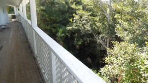 Une terrasse en bois couverte, dotée d’une balustrade blanche, et entourée d’une végétation luxuriante.