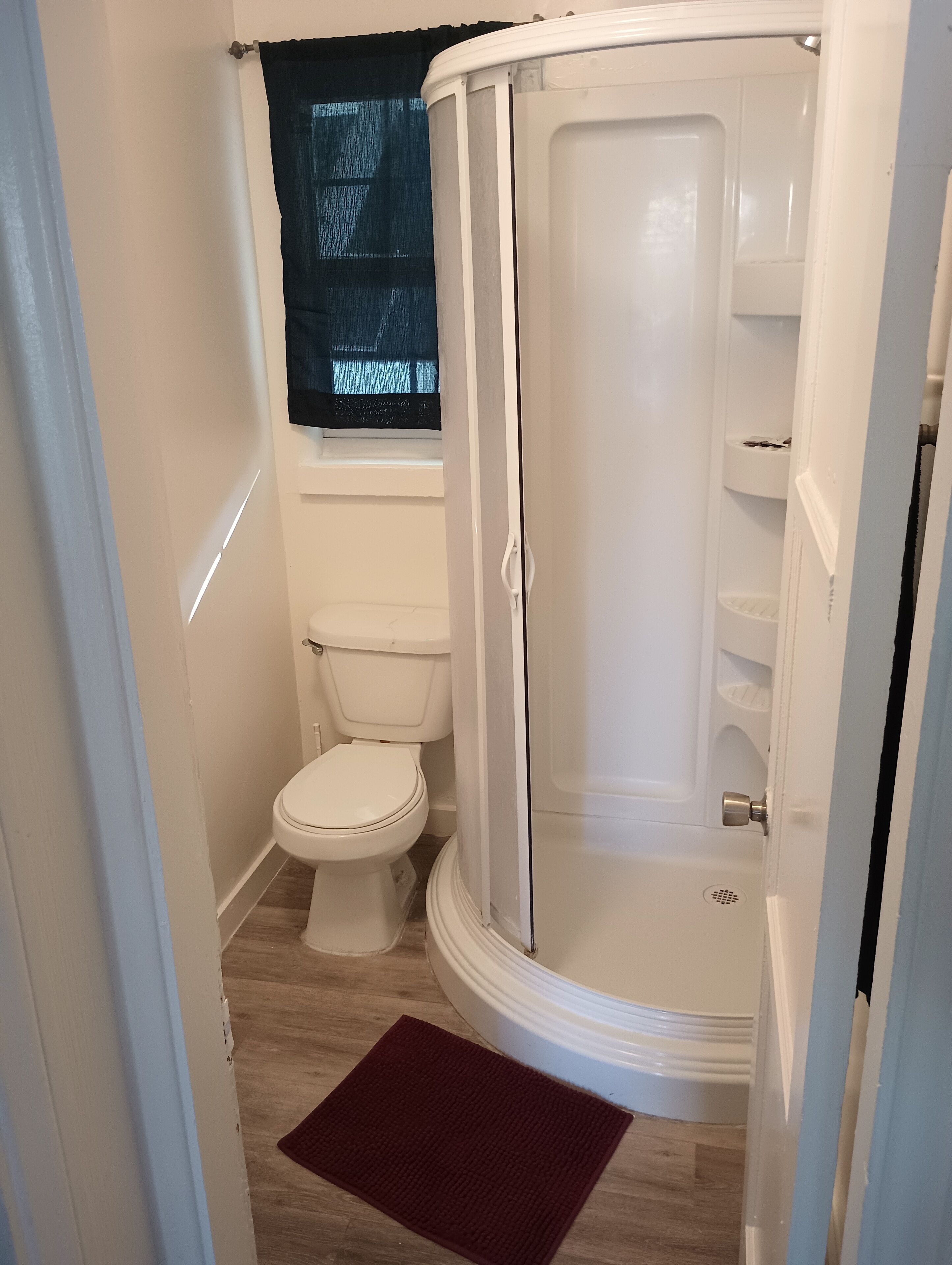 A compact bathroom with a toilet, a shower enclosure, and a window with a curtain.