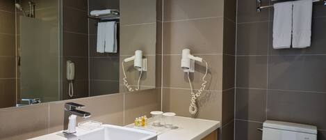 A modern bathroom with a large mirror, a white sink, a toilet, and two hair dryers mounted on the wall.