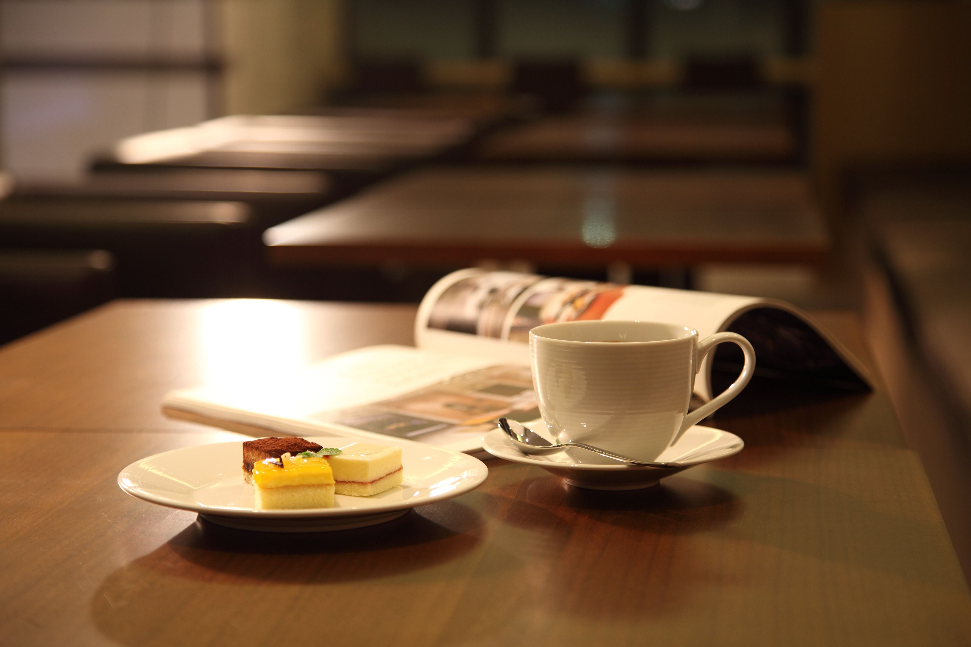A table with a white cup, saucer, and a small plate with a slice of cake.