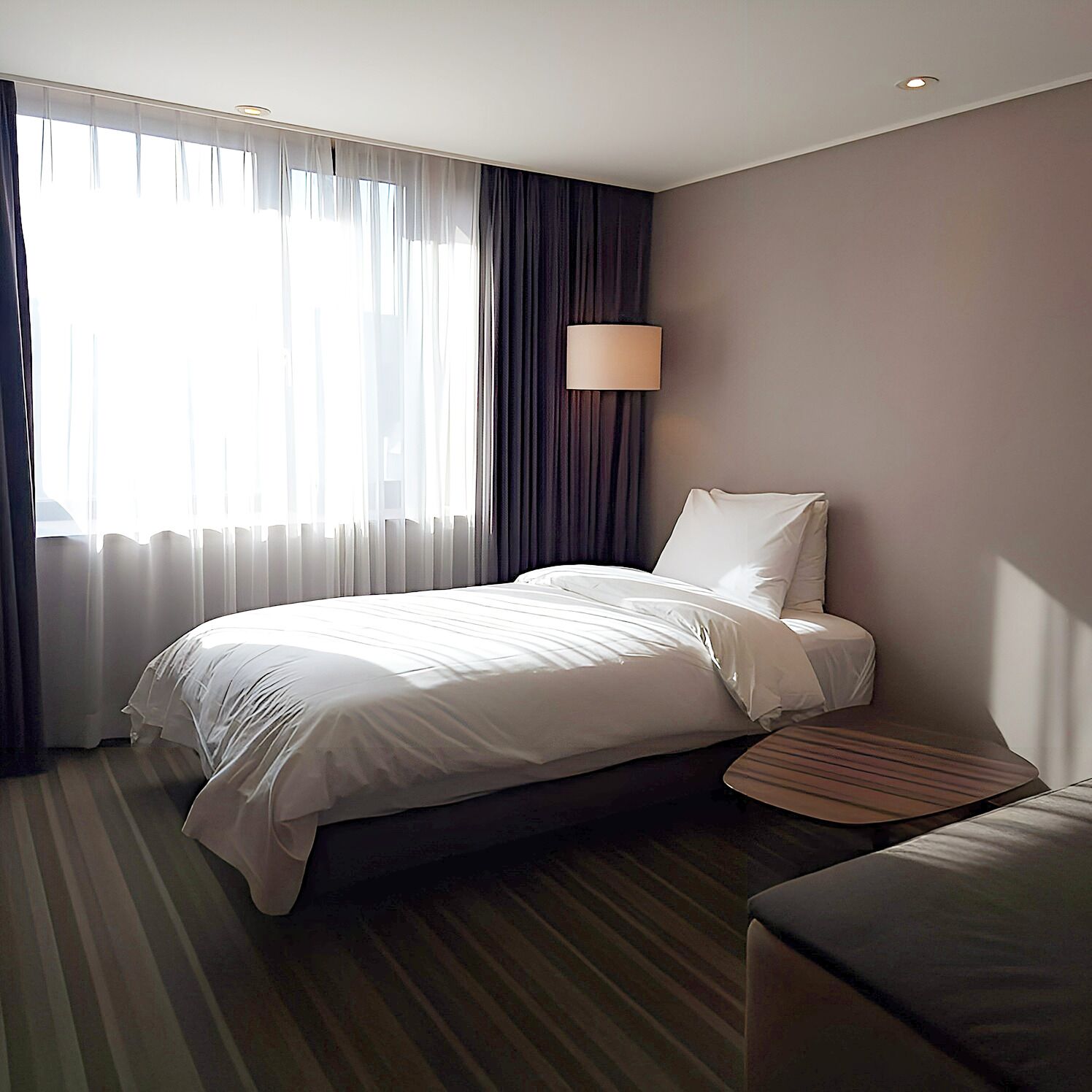 A hotel room with a bed, a bedside table, a lamp, and a window with curtains.