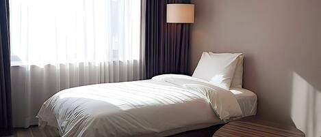 A hotel room with a bed, a bedside table, a lamp, and a window with curtains.
